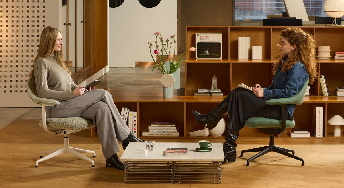 Two women sitting in a modern office setting, engaged in conversation.