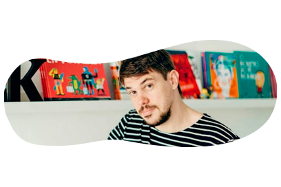 Person with striped shirt in front of colorful books on a shelf.