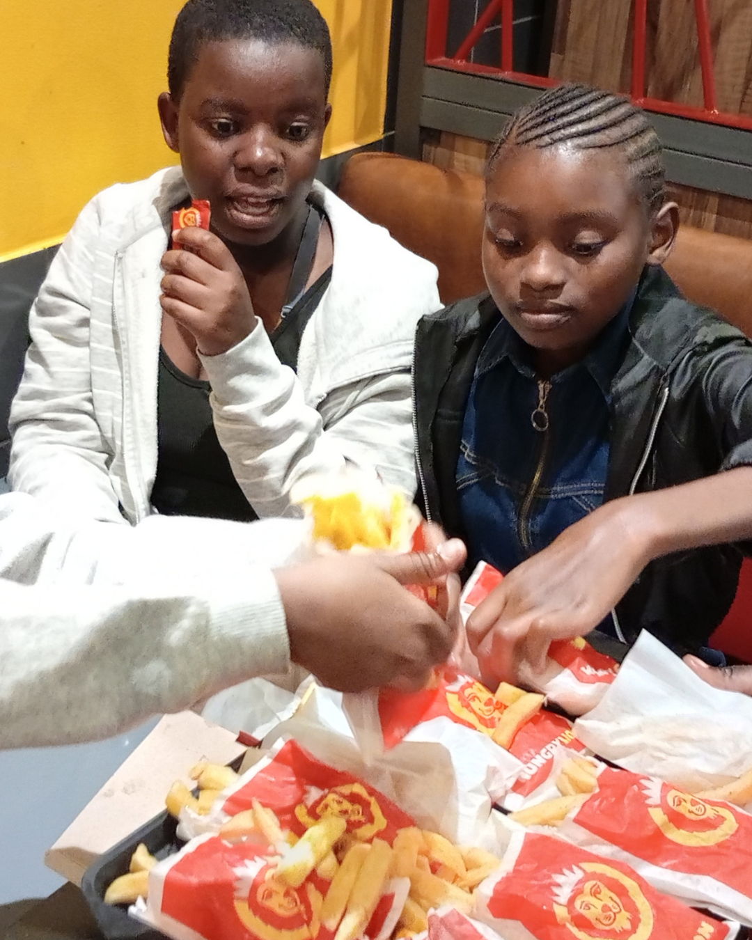 Two children sharing food at a table with takeaway packaging.