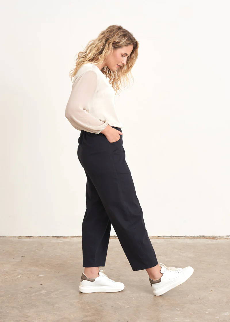 A model wearing a pair of dark blue loose fitting cropped trousers with an off white top