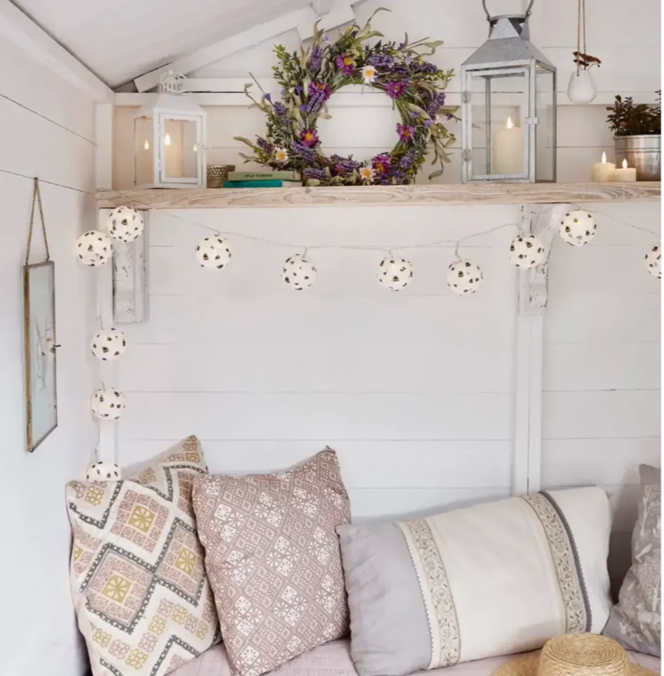 Bee fairy lights, floral spring wreath, lanterns and candles displayed inside summer house.