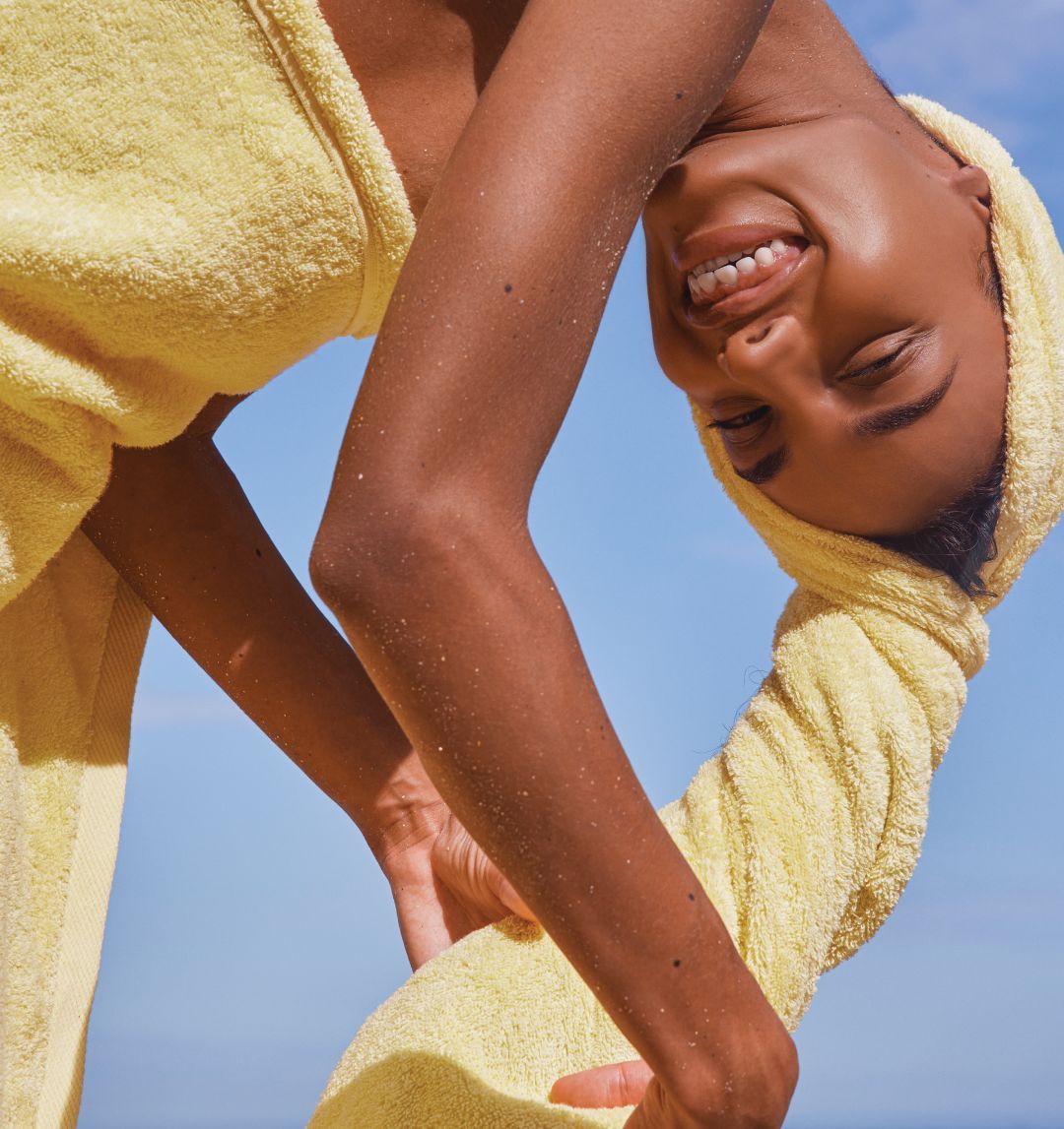 Smiling person in a yellow towel against a blue sky background.