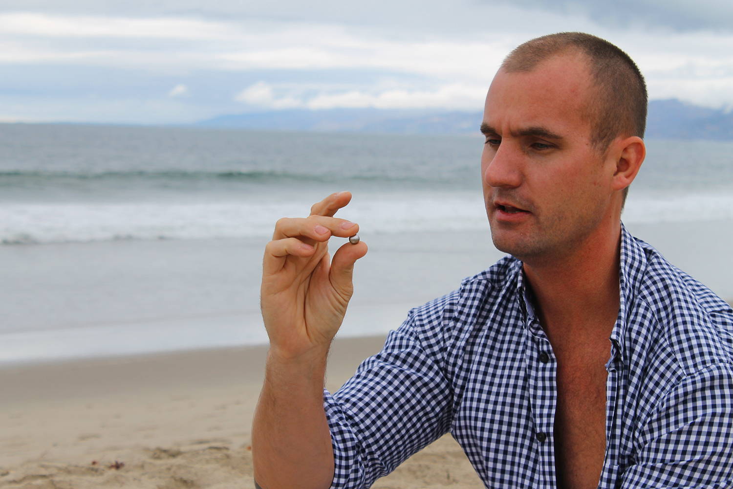 Owner of Pearls of Joy Kevin Canning examines a pearl with ocean in the background