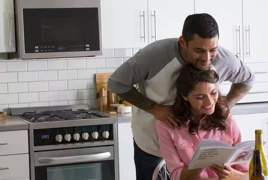 Man and woman looking at an appliance use and care manual in their kitchen.