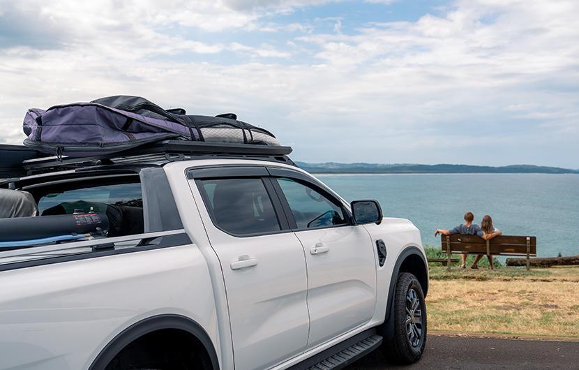 A ute with a Yakima Roof Rack LockNLoad Platform and Ruggedline, with surfboards, in front of the beach