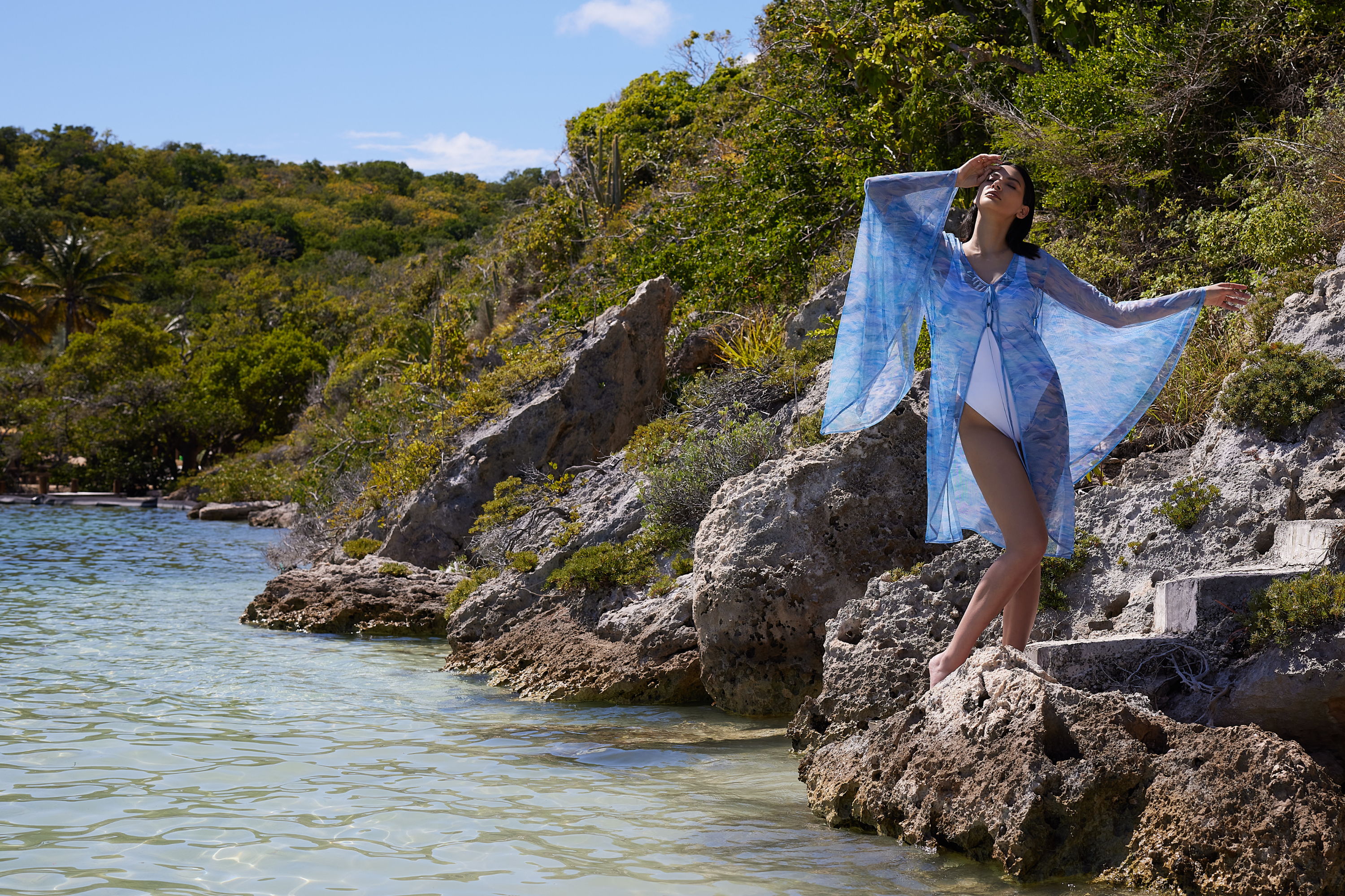 Person in a blue outfit poses on rocks by the water.