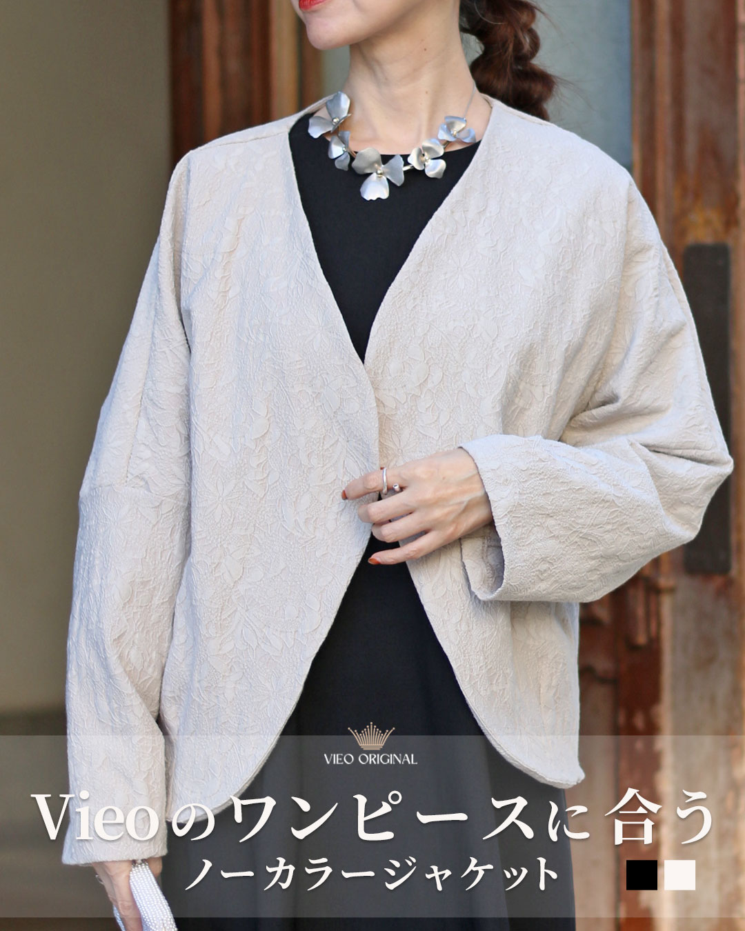 Woman wearing a light jacket over a black dress, with a statement necklace.