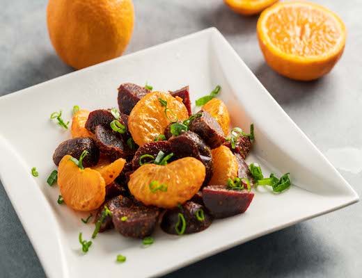 A plate of beets and mandarin oranges garnished with herbs.