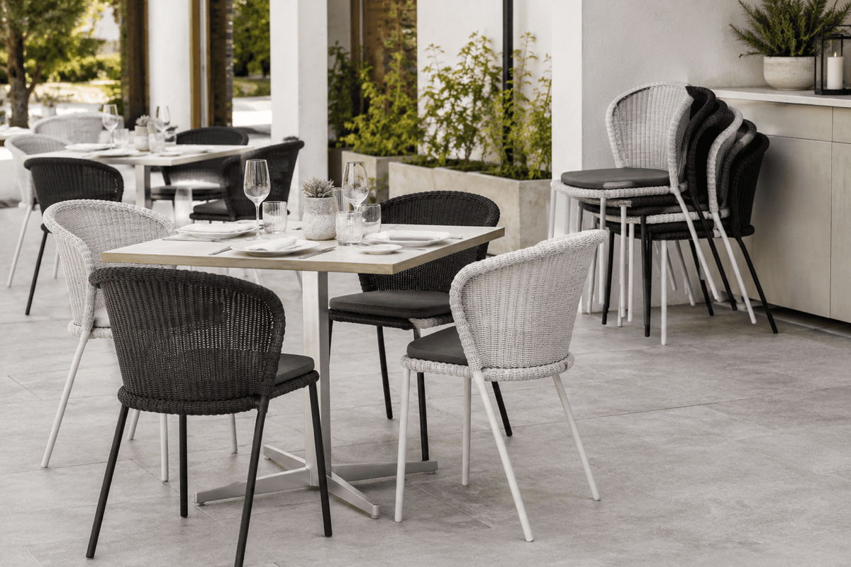 Stackable commercial outdoor dining chairs used at restaurant patio tables with additional chairs stored nearby
