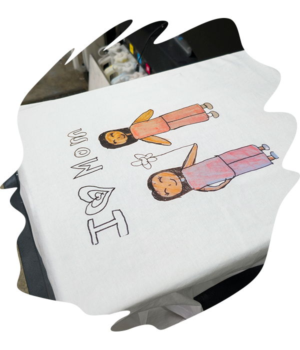 A printed white t-shirt on a printing platen showing a childrens hand drawn illustration of two figures with handwritten 