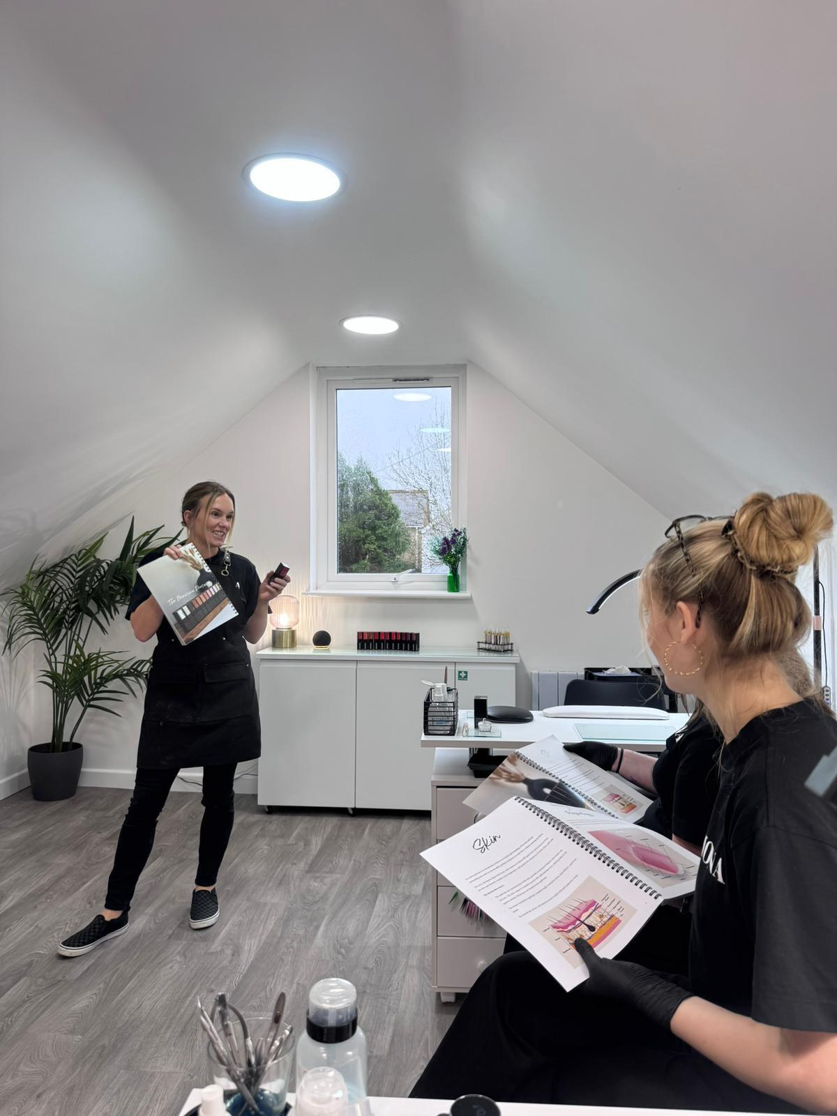 Two women in a modern salon, one presenting, the other reviewing material.