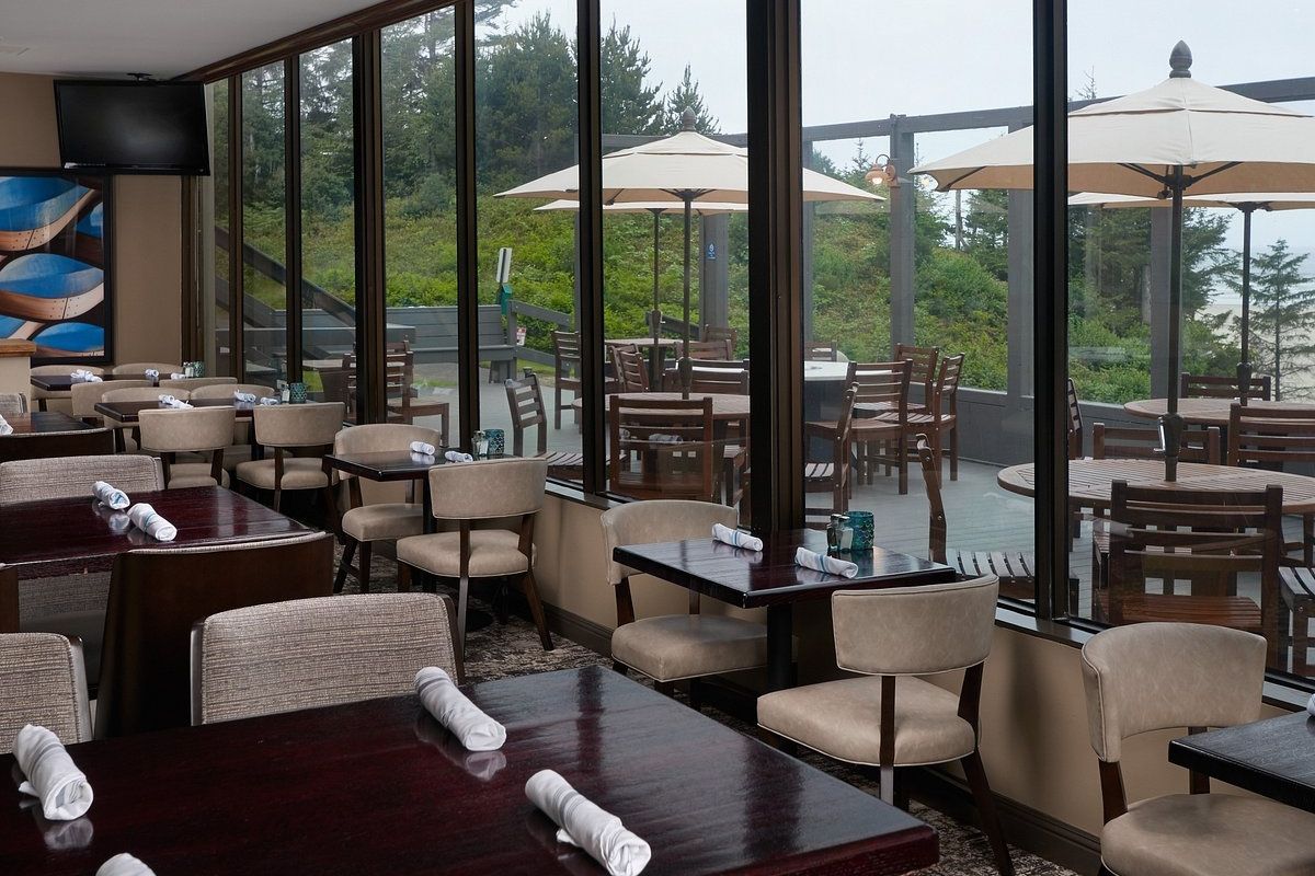 Modern restaurant interior with tables, chairs, and outdoor view through large windows.