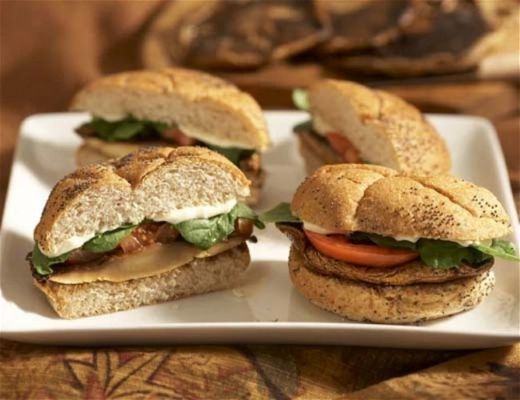 Four sandwiches with lettuce, tomato, and a whole grain bun on a plate.
