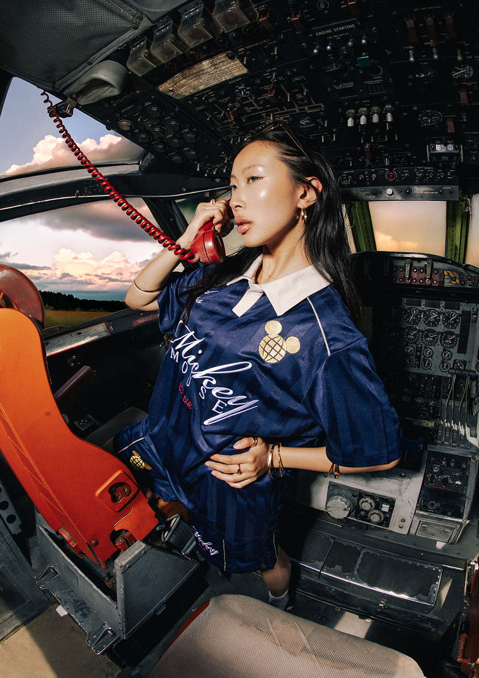 Person in a cockpit wearing a jersey, talking on a retro phone.