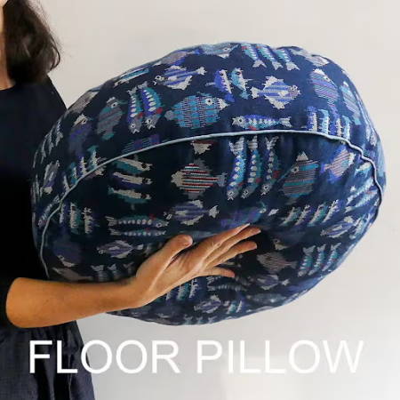 Women holding a big round hand-sewn floor pillow in blue fabric with prints