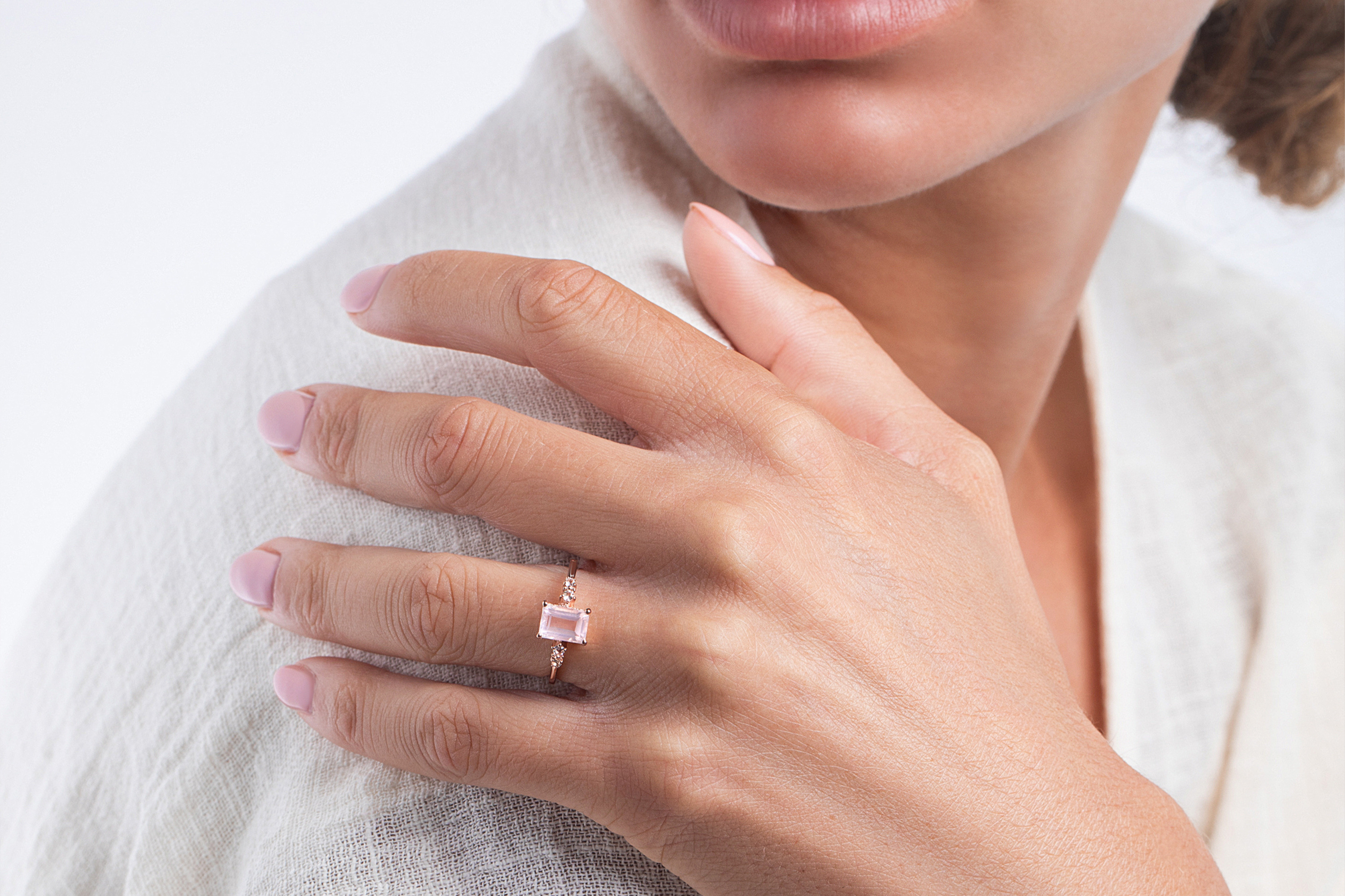 A woman is holding her shoulder and wearing the Rose Quartz Ring Grazia on her finger.