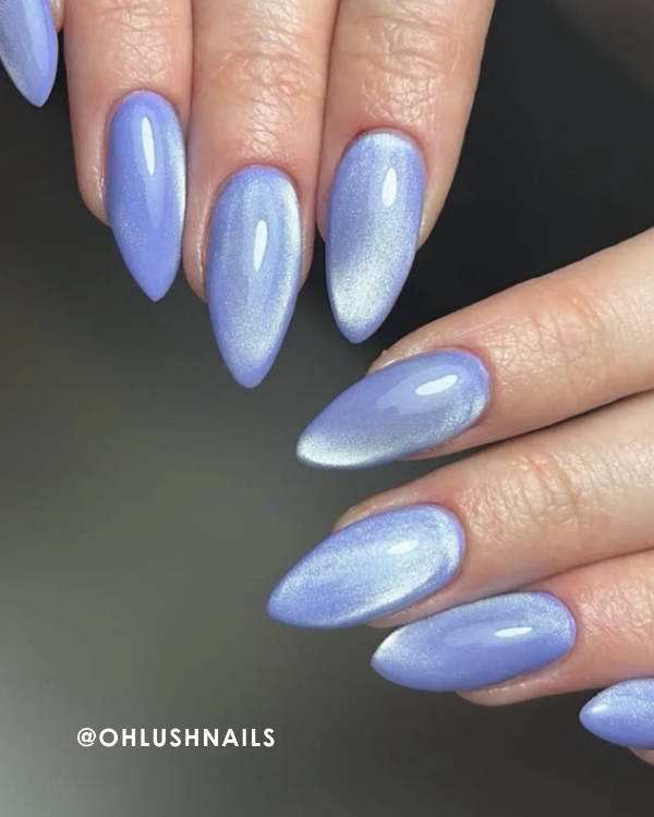 Hands with long, pointed lavender nails displayed on a neutral background.