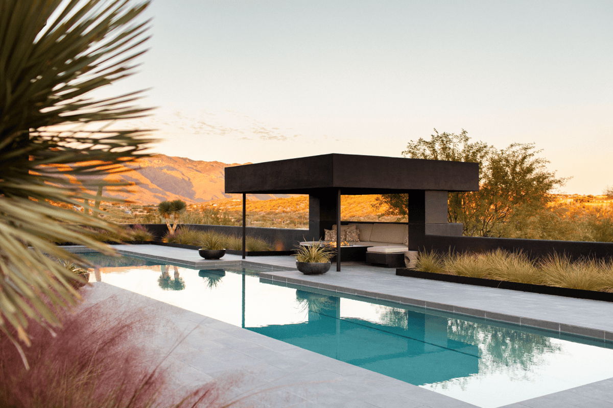 Modern Arizona pool and outdoor lounge pavilion at golden hour, showing desert landscaping, poolside seating, and a shaded outdoor living area.