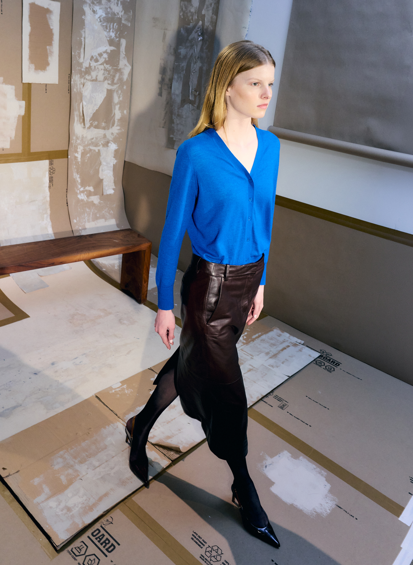 Model walking on a runway in a blue top and black skirt.