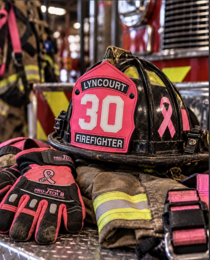 Pink firefighter gear including helmet and gloves on a metallic surface.