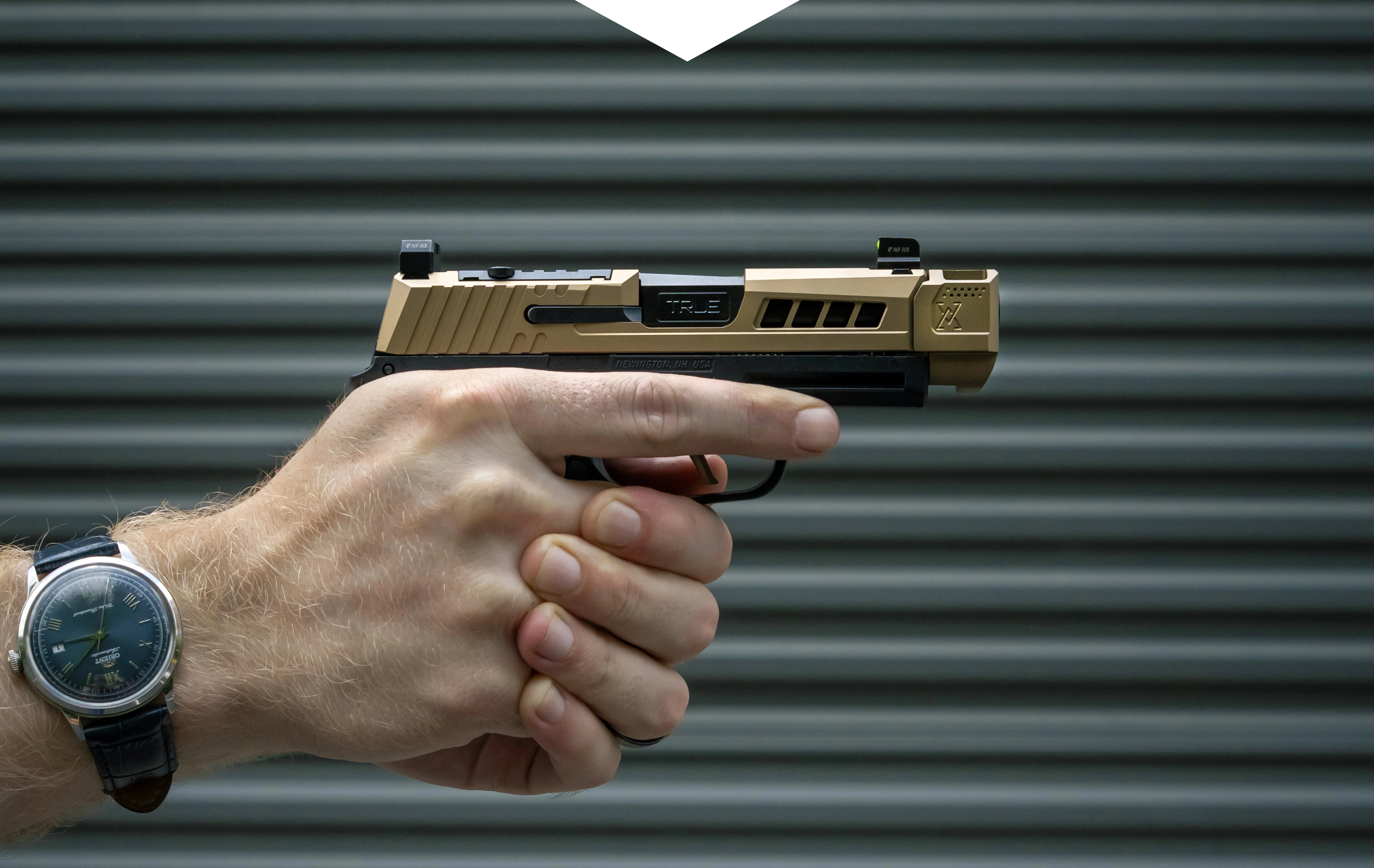 Hand holding a gold and black handgun with a watch on wrist.