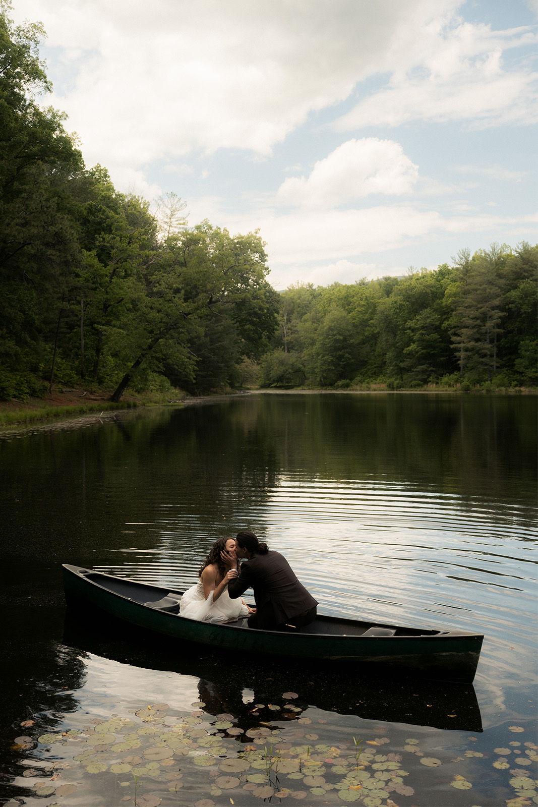Couple in a boat on a serene lake surrounded by trees.