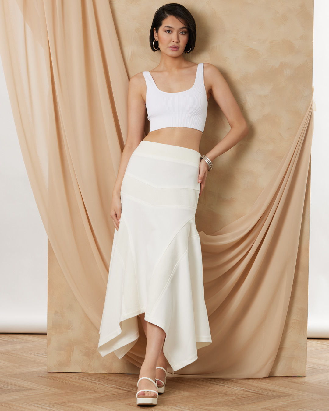 Woman in a white crop top and skirt against a neutral backdrop.