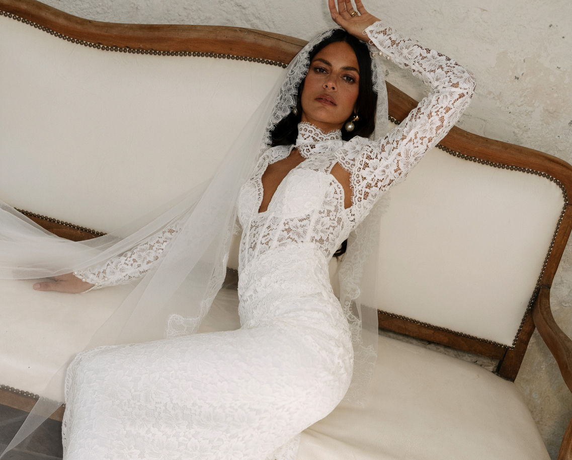 A woman in a white wedding dress poses on a sofa.