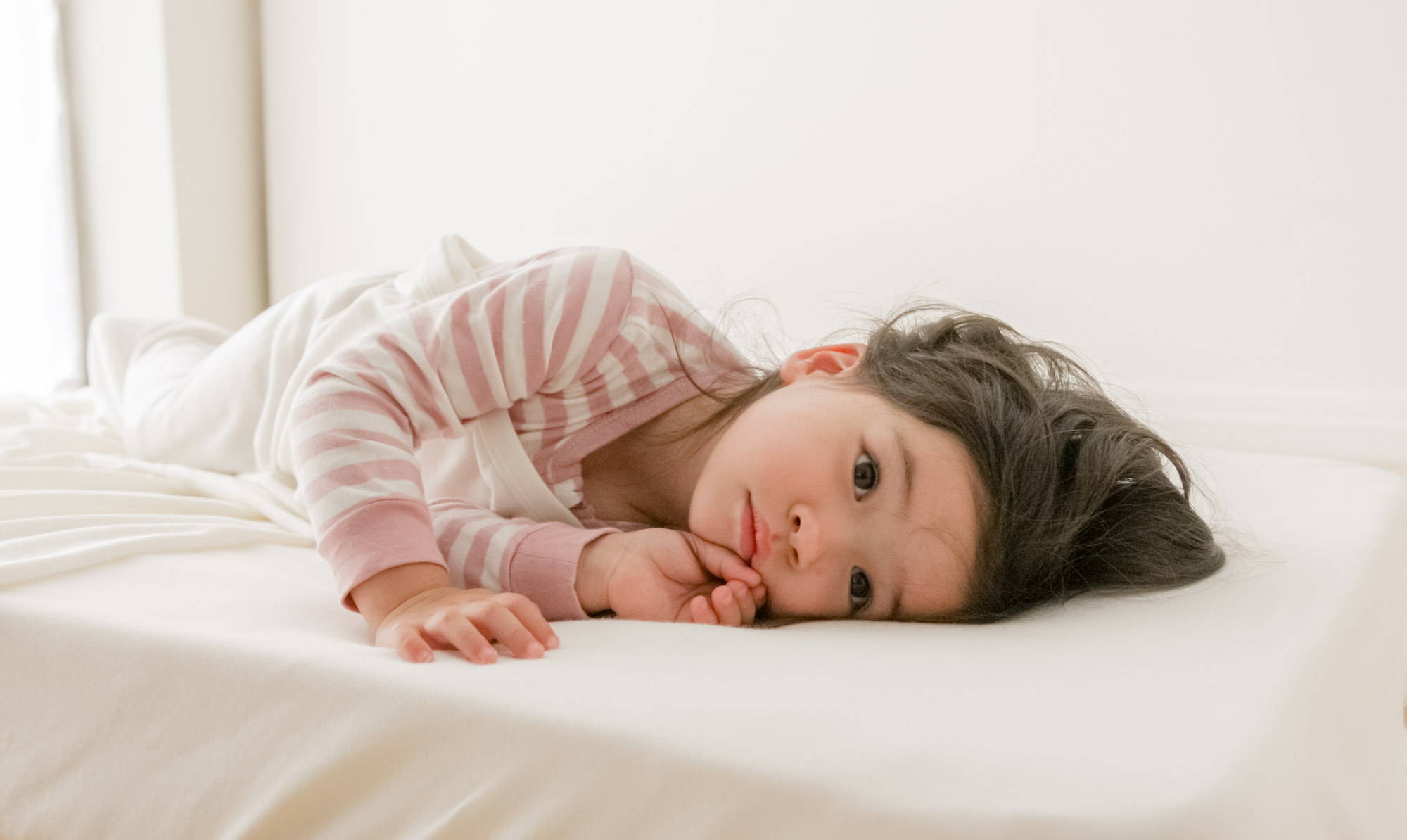 Toddler lying on side in bed wearing Woolbabe pyjamas