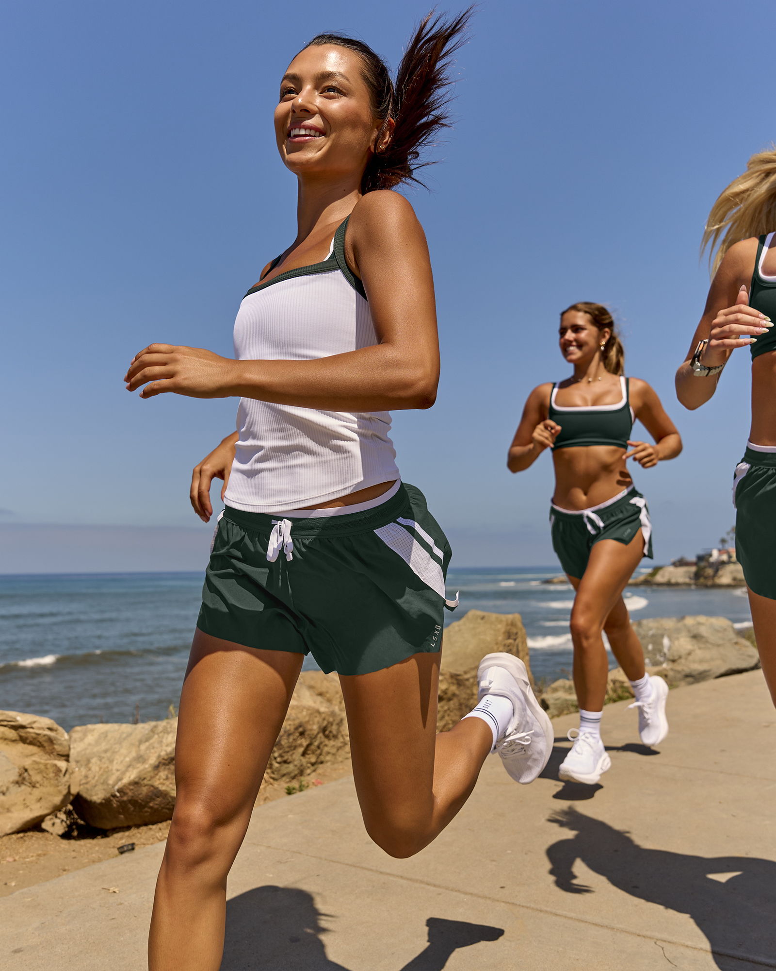 Three women jogging along a coastal path on a sunny day.