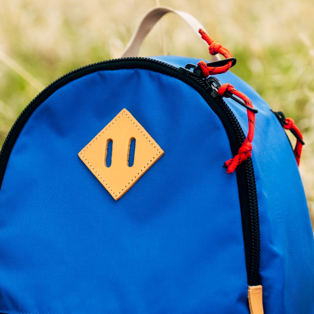 Blue backpack with a diamond-shaped leather patch and red zipper pulls.