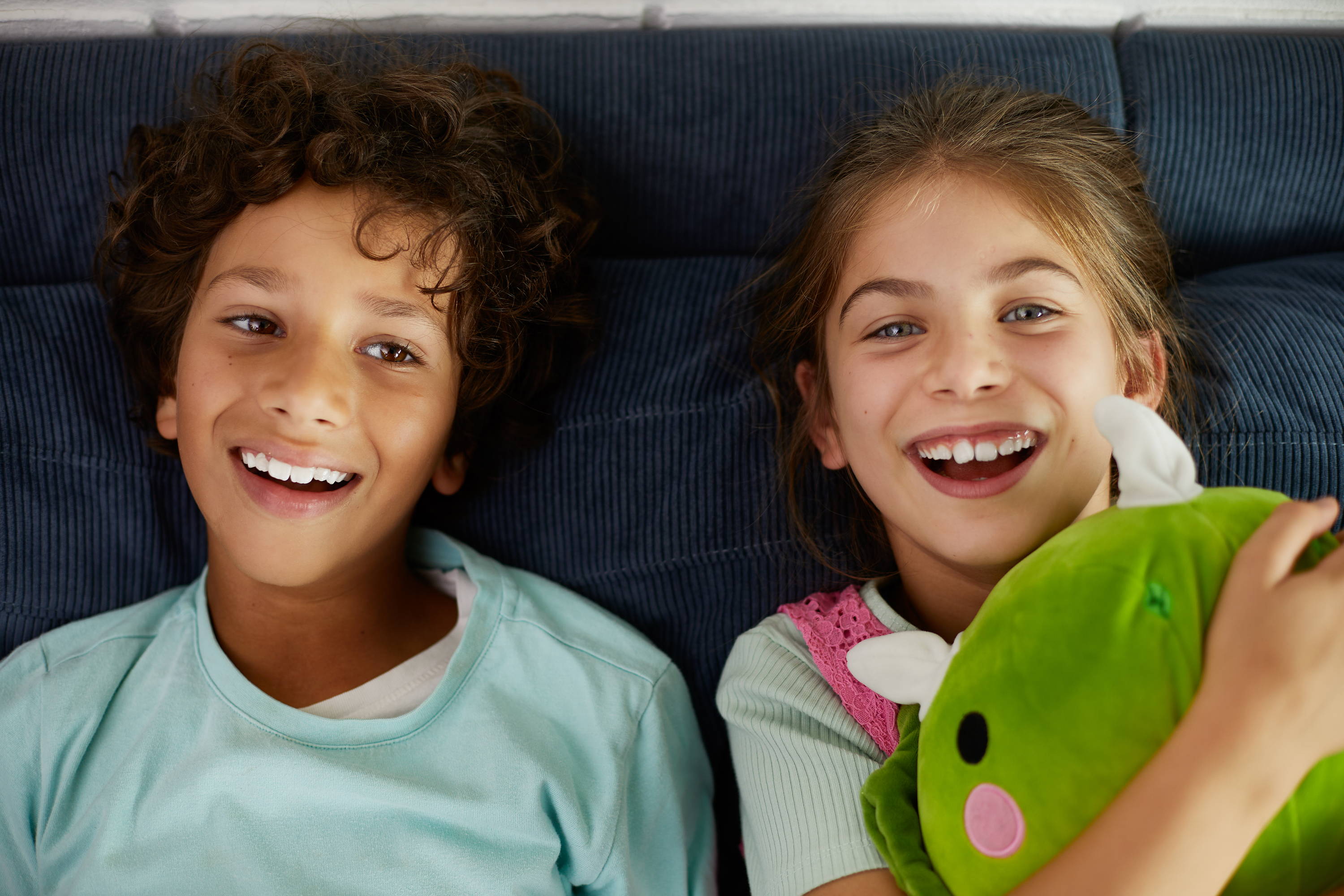 Lachende jongen en meisje op een blauwe bank binnen in huis. Allergie kan het voor kinderen een stuk lastiger maken om zich goed te voelen.