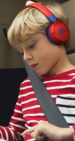 Boy wearing red headphones, seated in a car with a seatbelt.