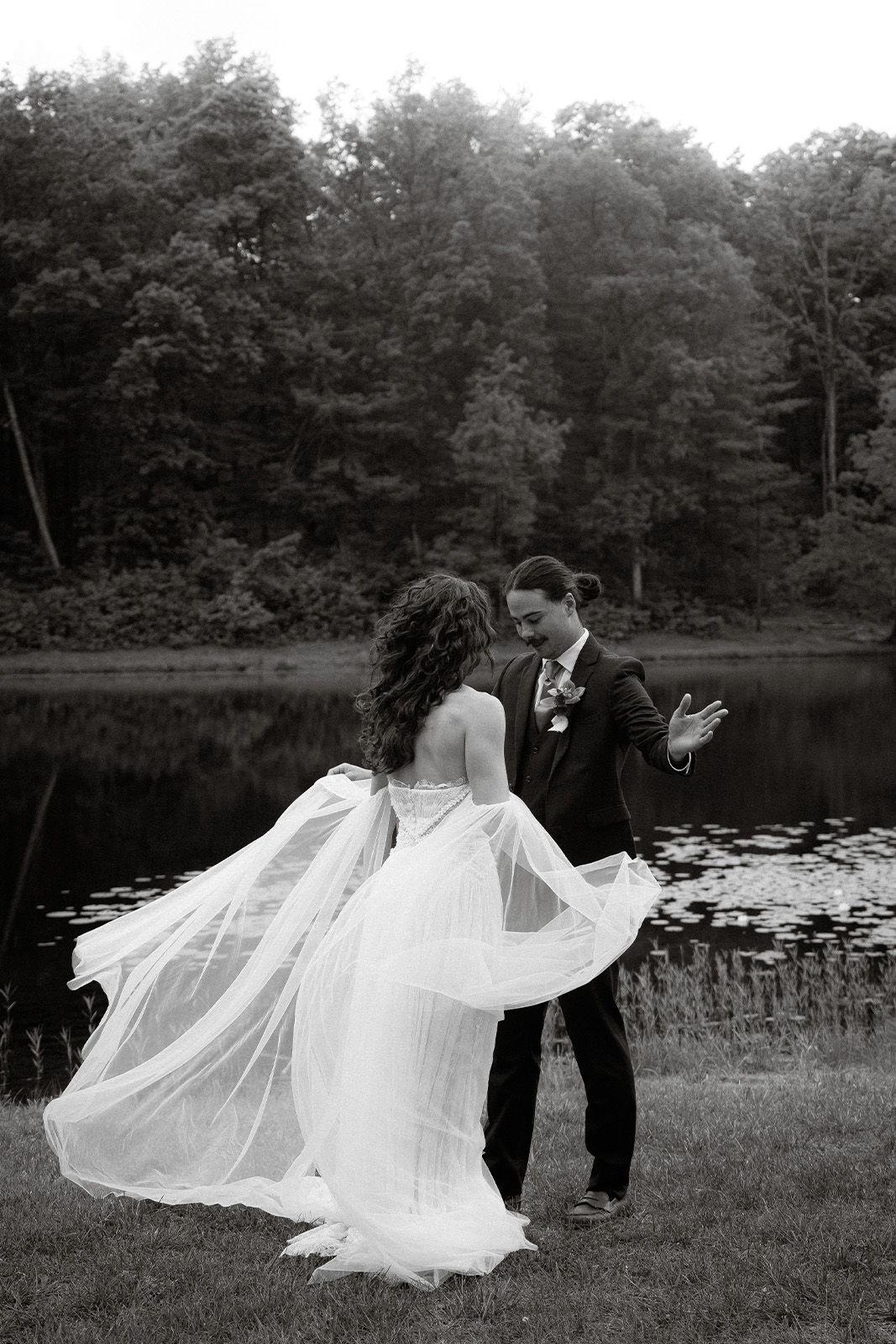 Couple dancing by a lake, surrounded by trees, in black and white.