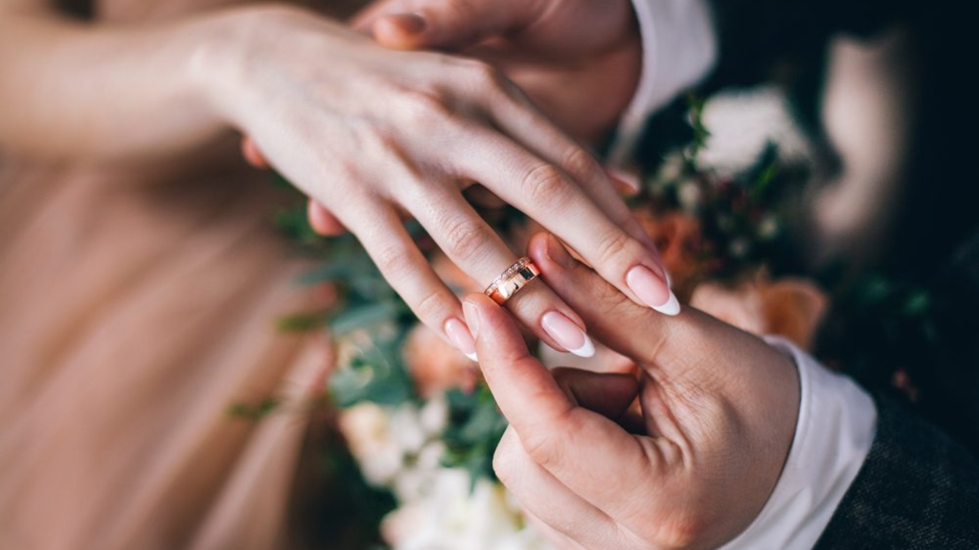 Close-up of bride’s hand with elegant wedding nails and a wedding band showcasing a bridal manicure
