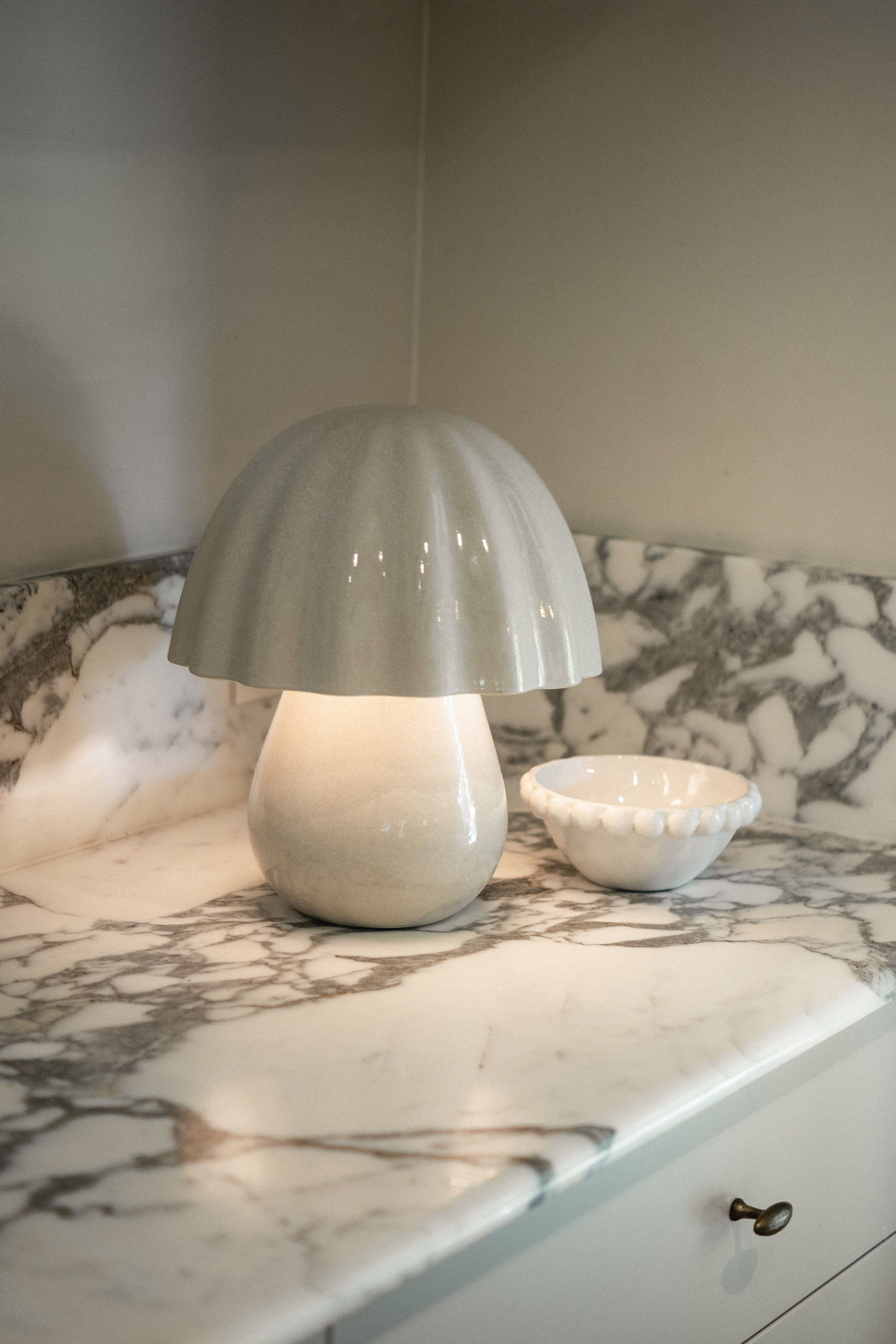 A white lamp on a marble countertop next to a small bowl.