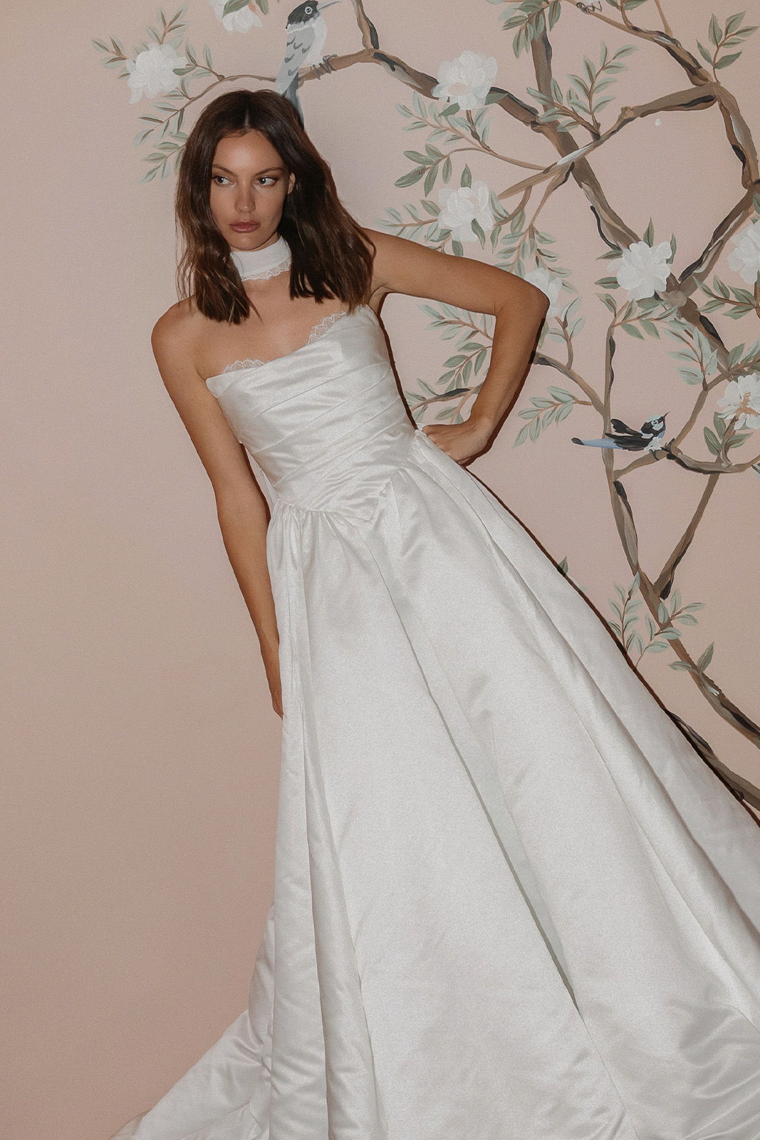 Model wearing a strapless white gown against a floral background.