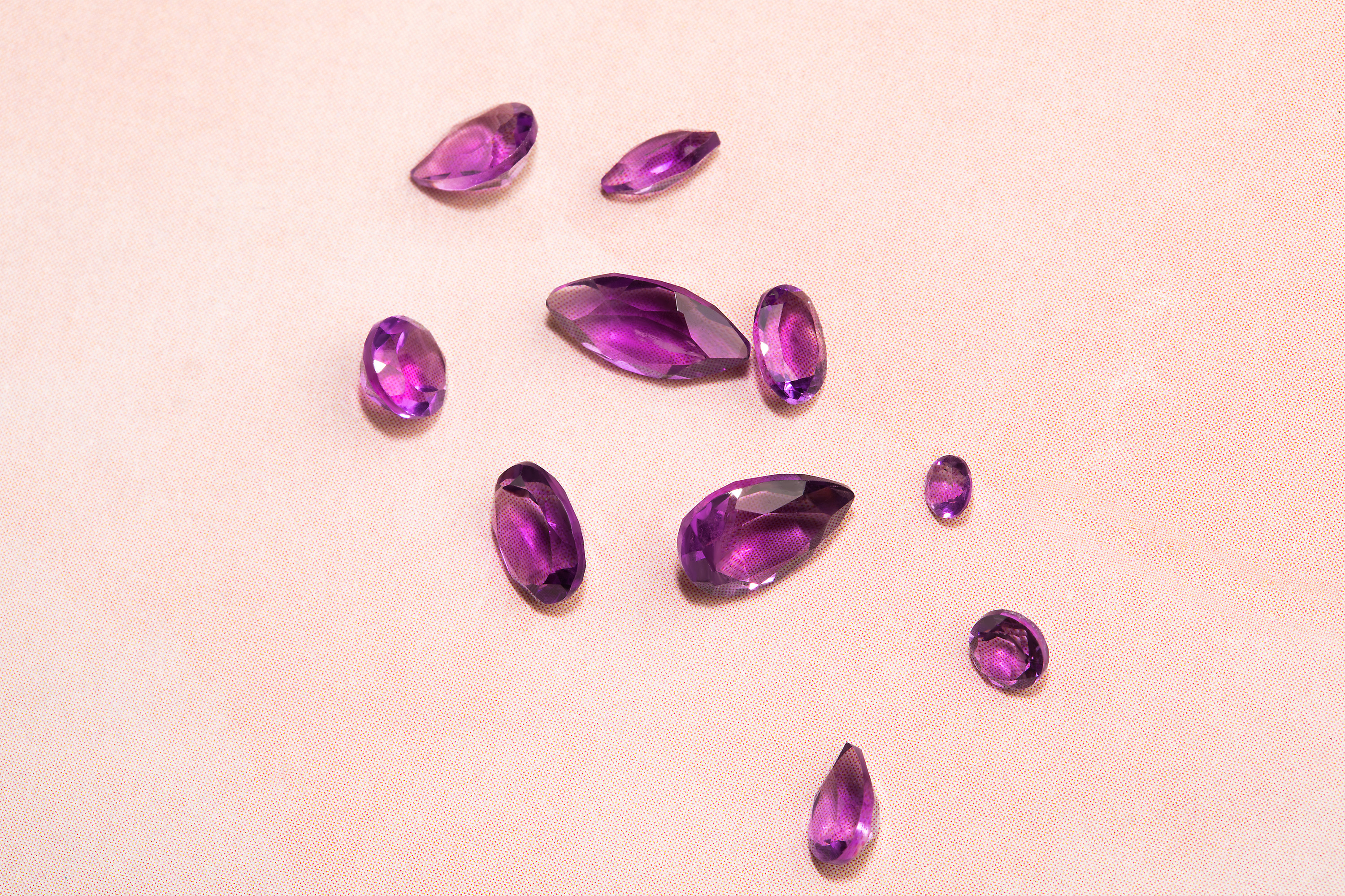 Authentic Amethyst gemstones are lying on a rose surface.