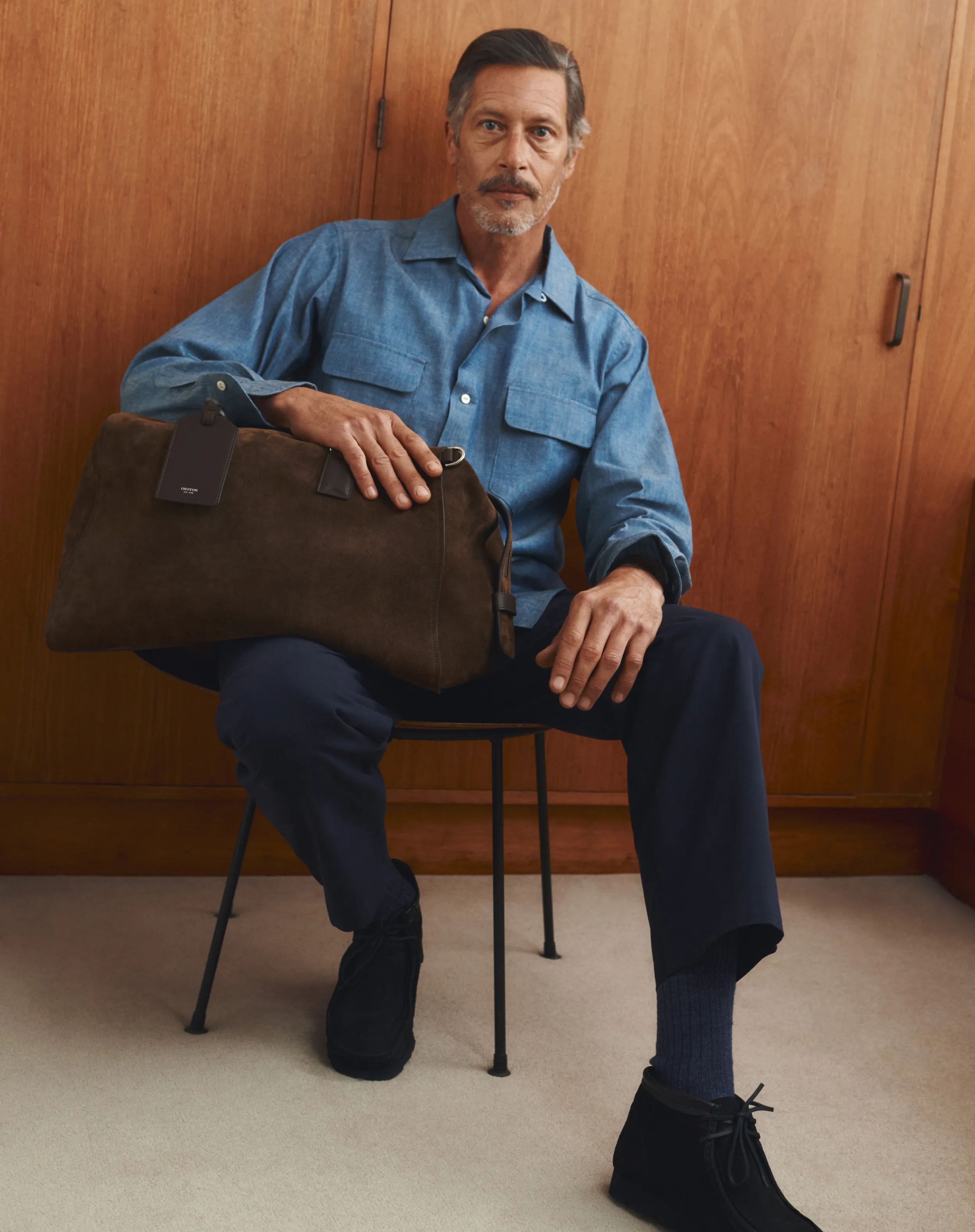 Man sitting on a chair, holding a bag, wearing casual attire.
