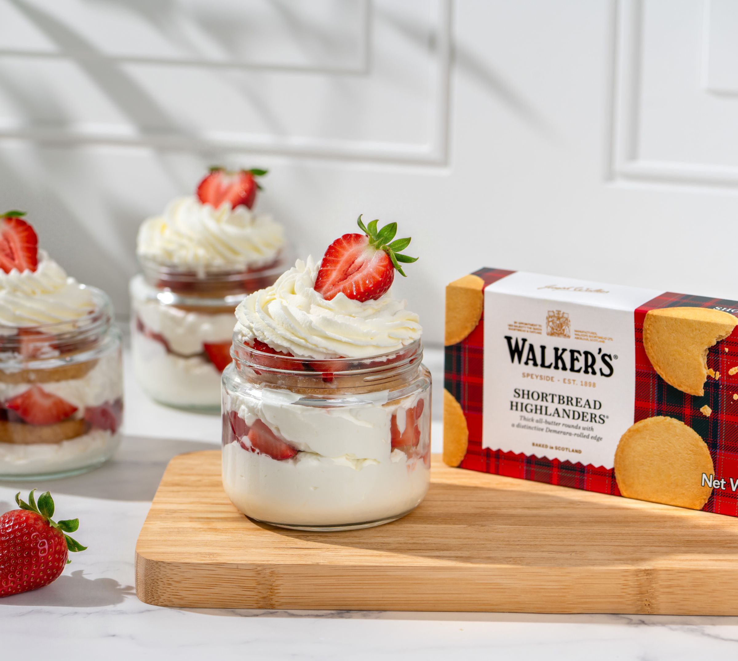 Dessert jars with strawberries and cream next to a box of cookies.