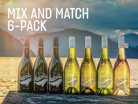 Six The Hidden Sea wine bottles lined up on a rocky ledge by the water at sunset, with ‘MIX AND MATCH 6-PACK’ text.