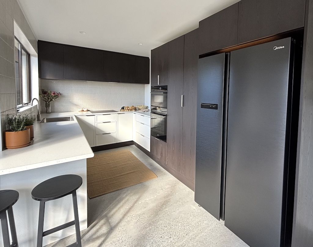 Modern kitchen with dark cabinets, white countertops, and a black refrigerator.