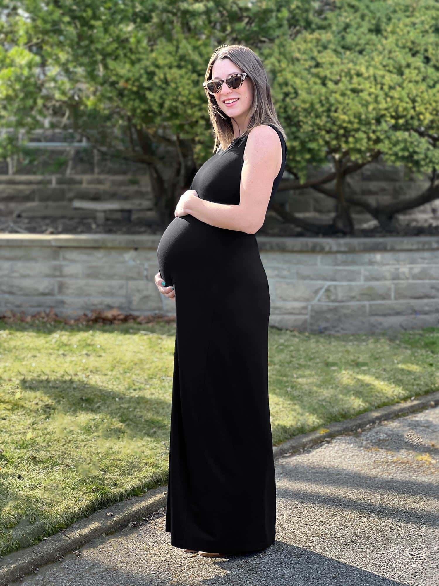Pregnant woman standing wearing Miik's Prisha reversible maxi dress in black.