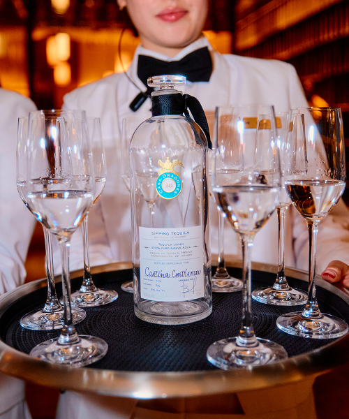 A waiter holding a tray with glasses and a bottle of water.