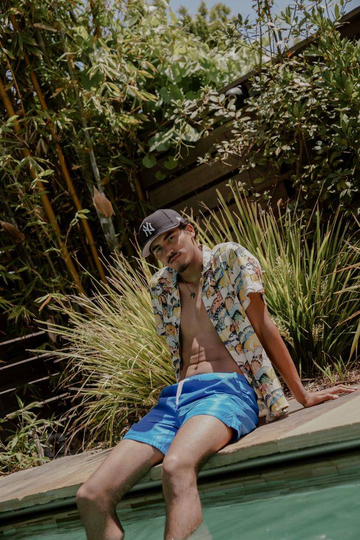 male model wearing maison article button up and shorts sitting by pool