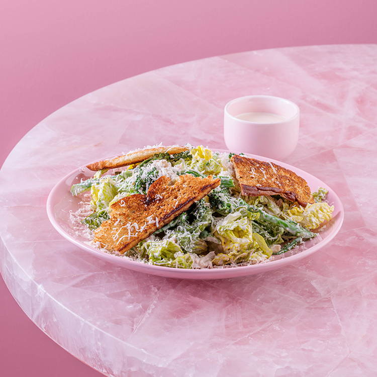 Chicken Caeser salad with foccacia bread croutons on pink background