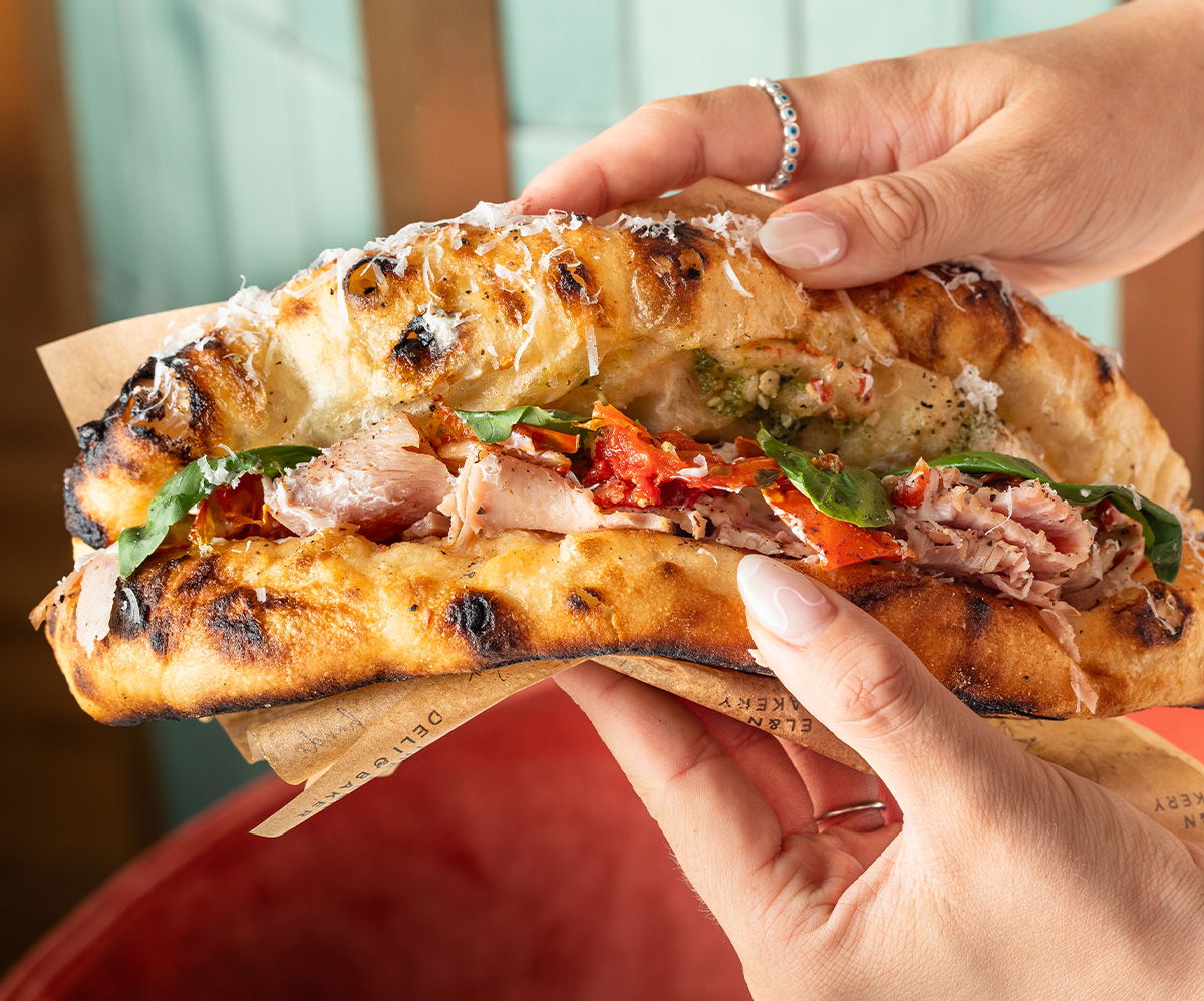 A person holding a large, filled sandwich with various toppings.
