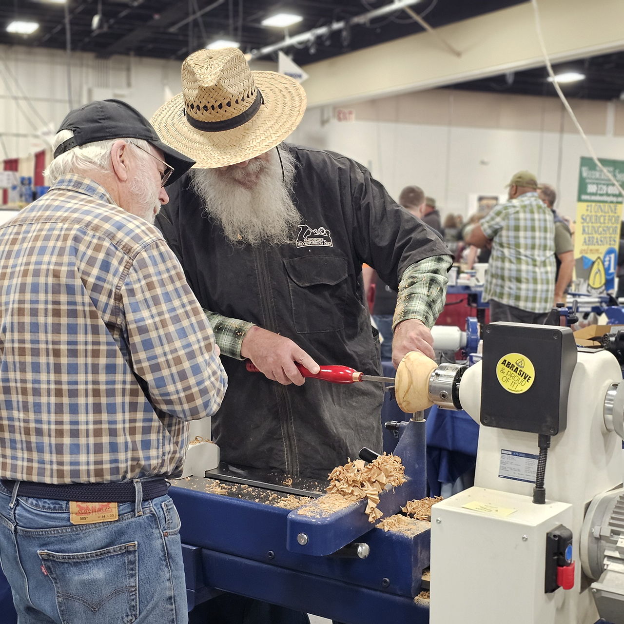 Two men working with a wood lathe at a craft fair.