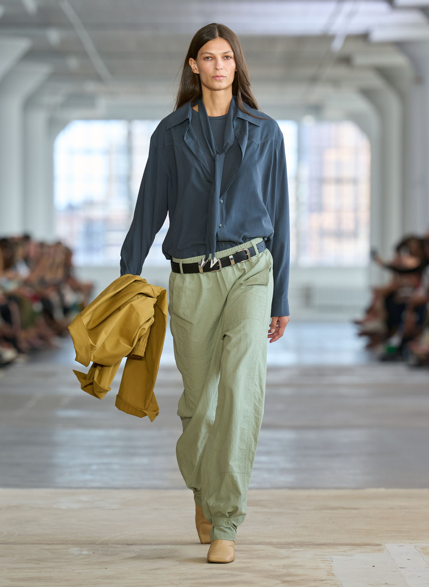 Model walking down runway wearing casual outfit with oversized shirt and trousers.