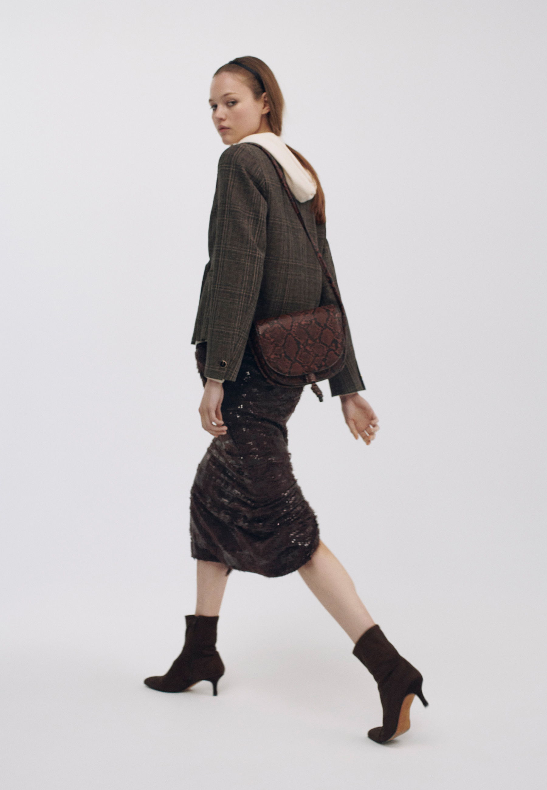 Model walking in stylish outfit with handbag and ankle boots.